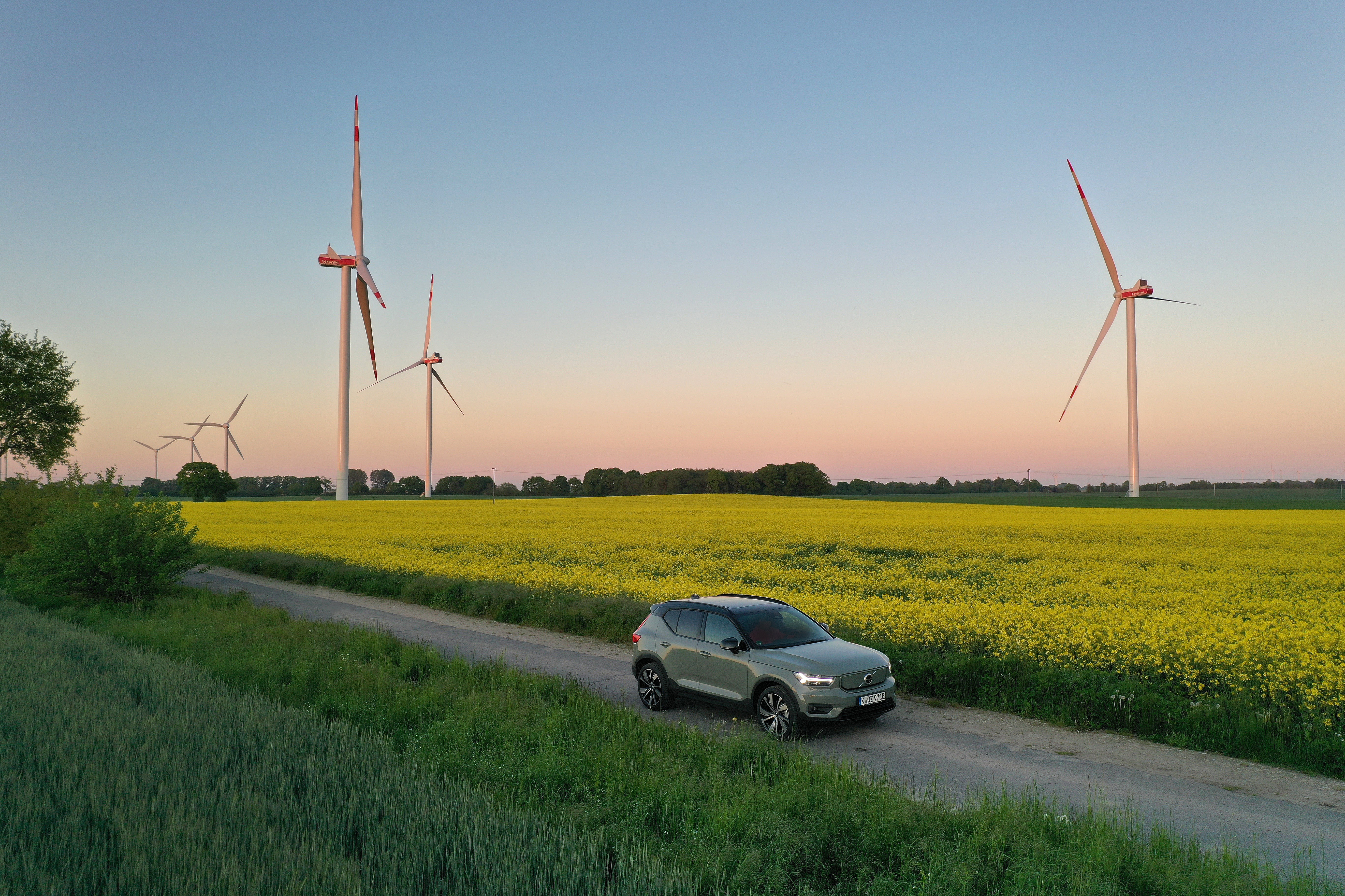 elektrische auto rijdt op een landweg met velden en windmolens erachter