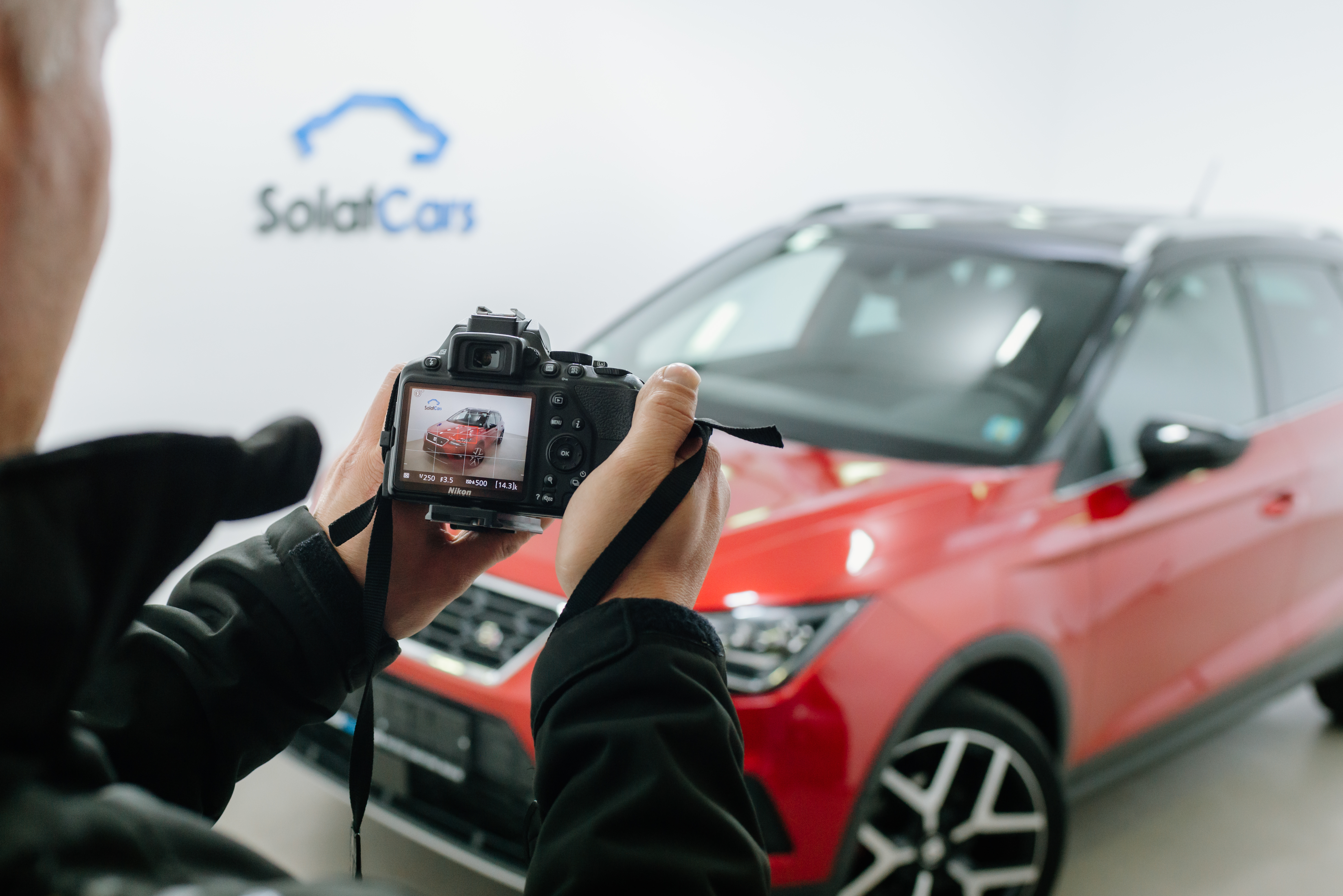 Close up van een man die met een dslr-camera een foto maakt van een rode auto in een fotostudio